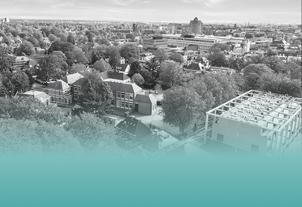 Dronebeeld van woonwijk met veel bomen en skyline van Arnhem op de achtergrond